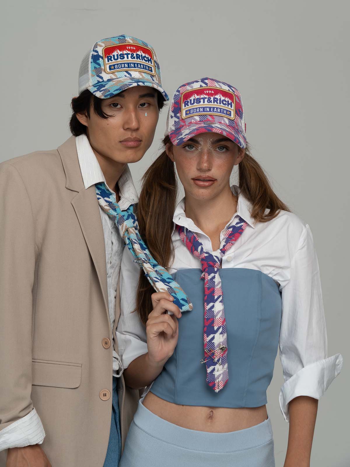 Two people wearing Born In Earth Blue & Pink Trucker Hats on a gray background.