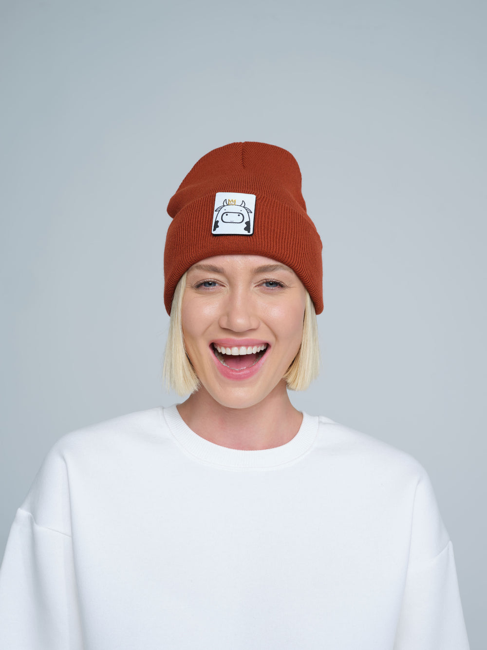 Person wearing a brown beanie with a logo on a plain background