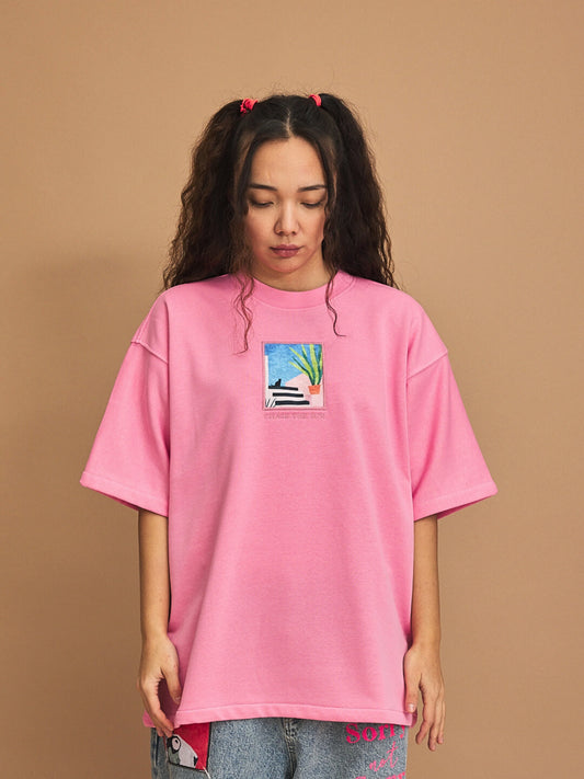 Person wearing a pink t-shirt with a graphic design on a brown background