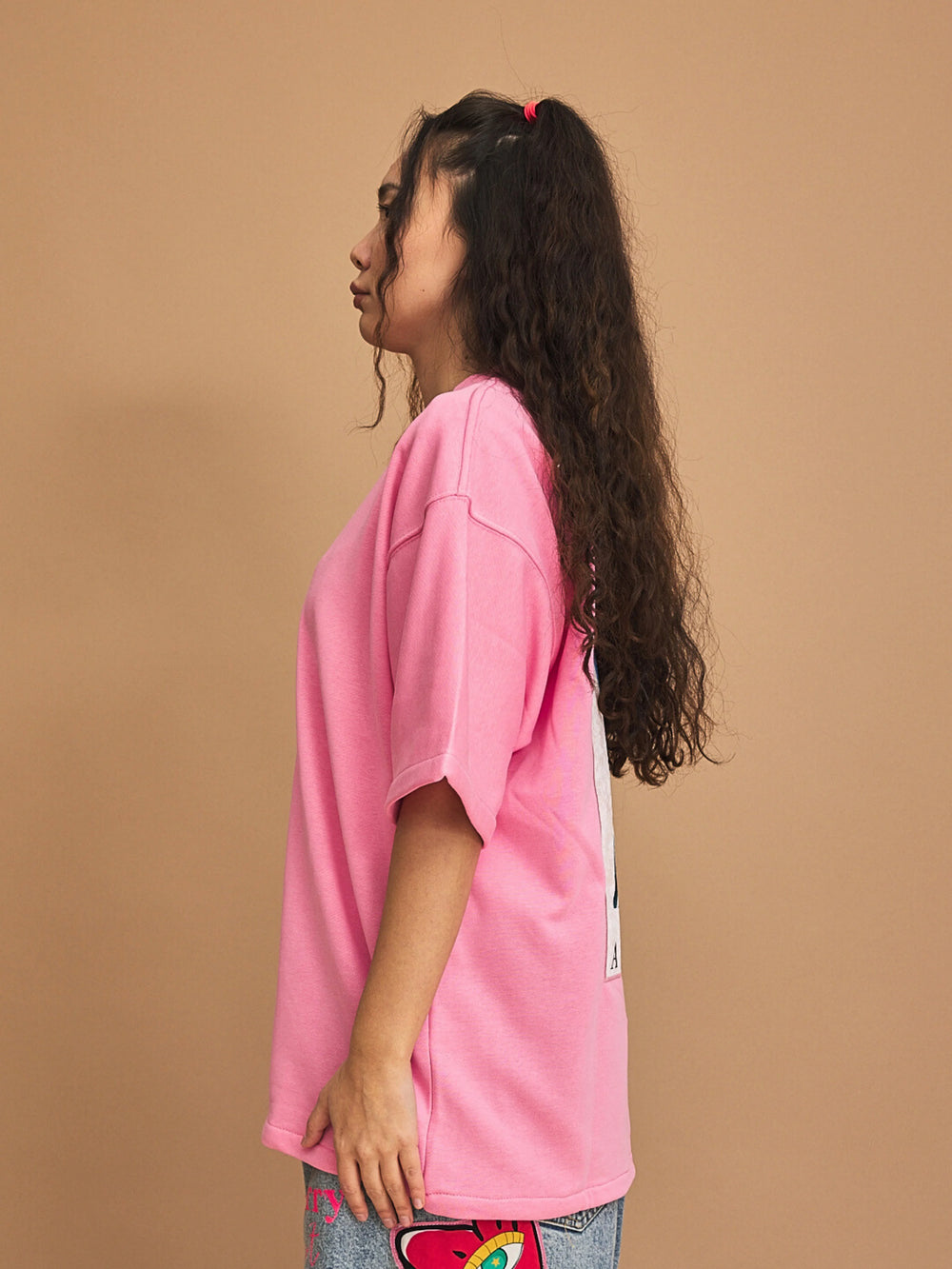 Person wearing a pink oversized t-shirt with a white stripe on a brown background