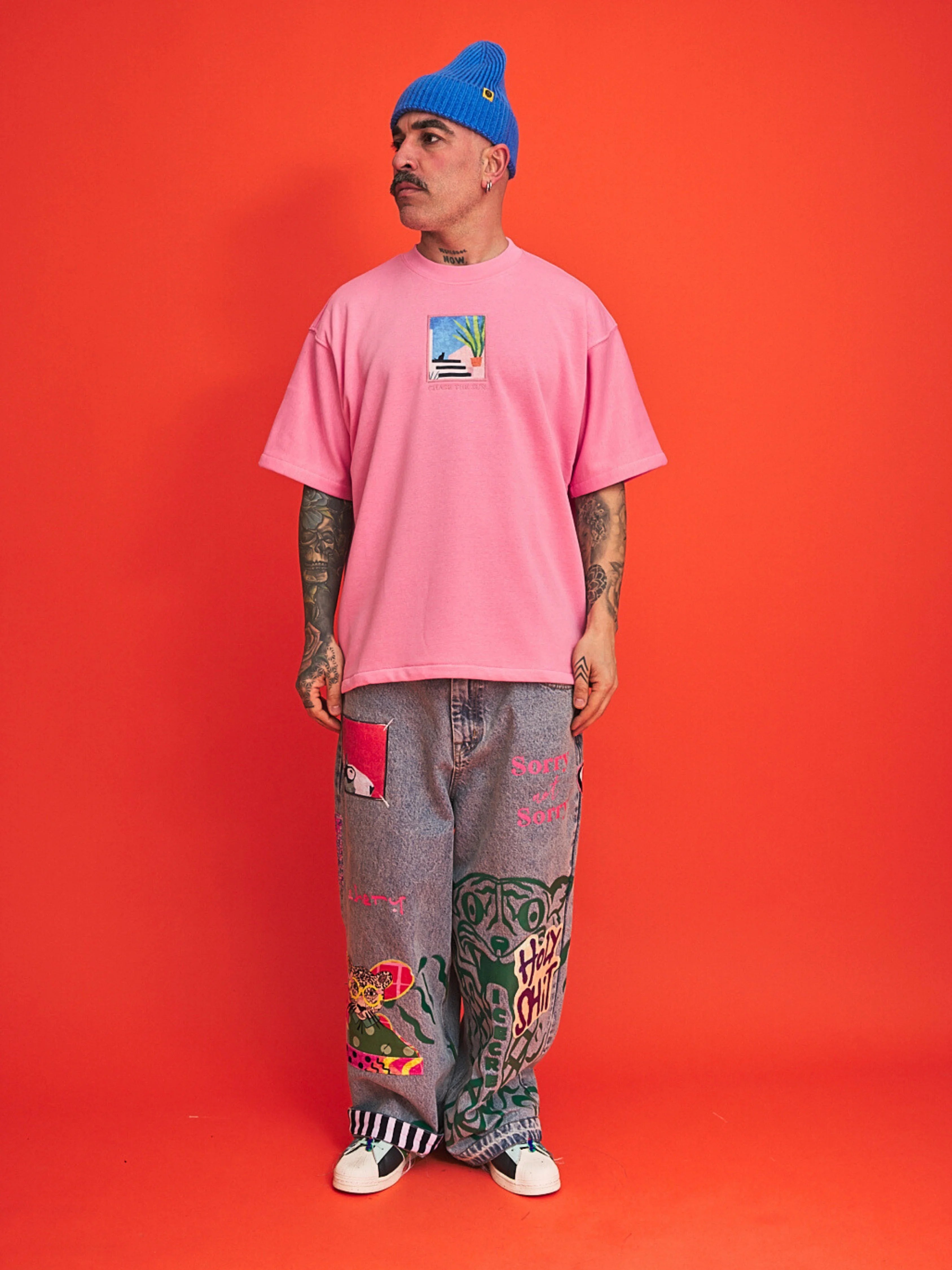 Person wearing a pink t-shirt and colorful pants against an orange background