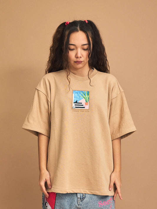 Person wearing a beige t-shirt with a graphic design on a brown background
