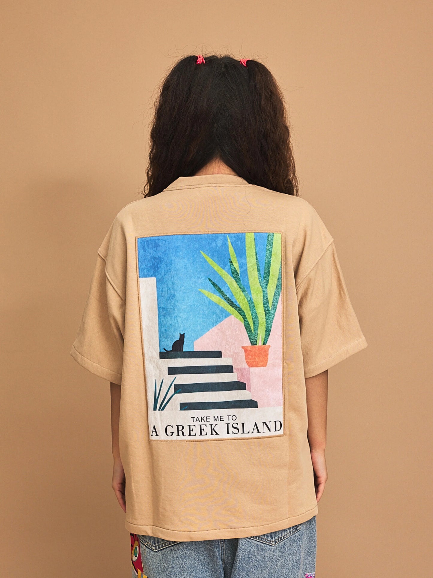 Person wearing a beige t-shirt with a graphic design on the back against a brown background