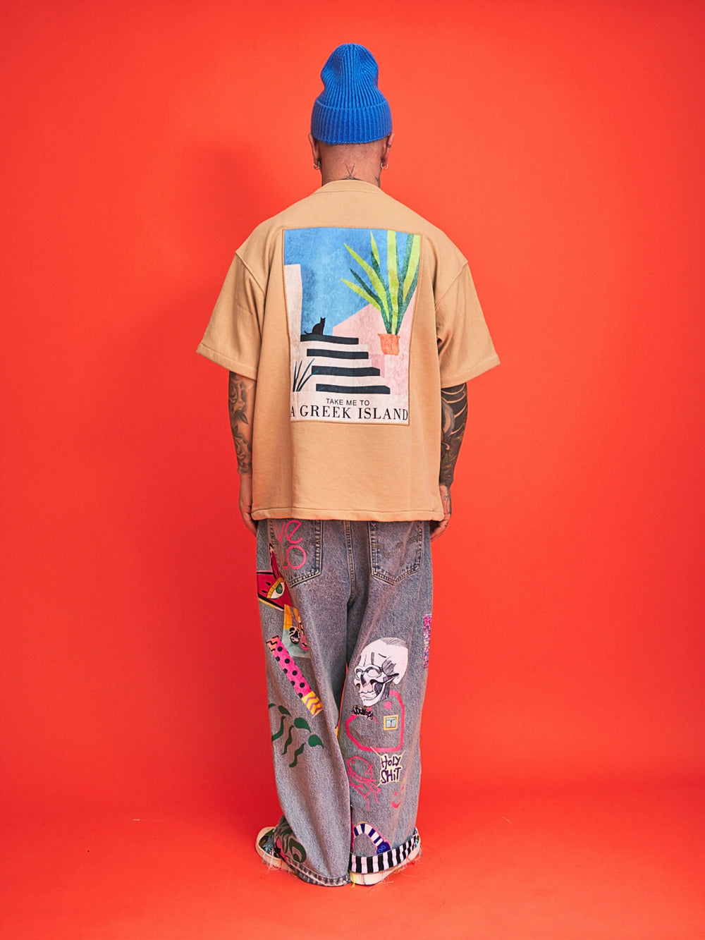 Person wearing a beige t-shirt with a colorful graphic and patterned pants on an orange background