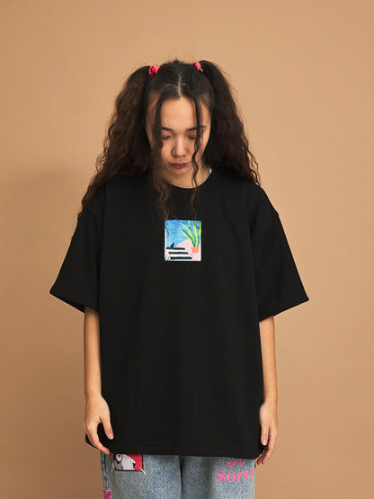 Person wearing a black t-shirt with a small graphic on a brown background