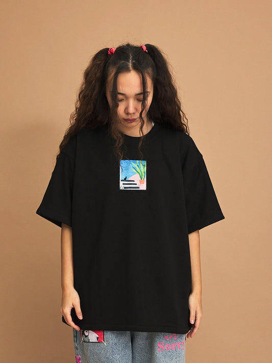 Person wearing a black t-shirt with a small graphic on a brown background