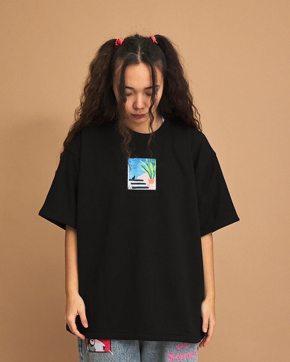 Person wearing a black t-shirt with a small graphic on a brown background