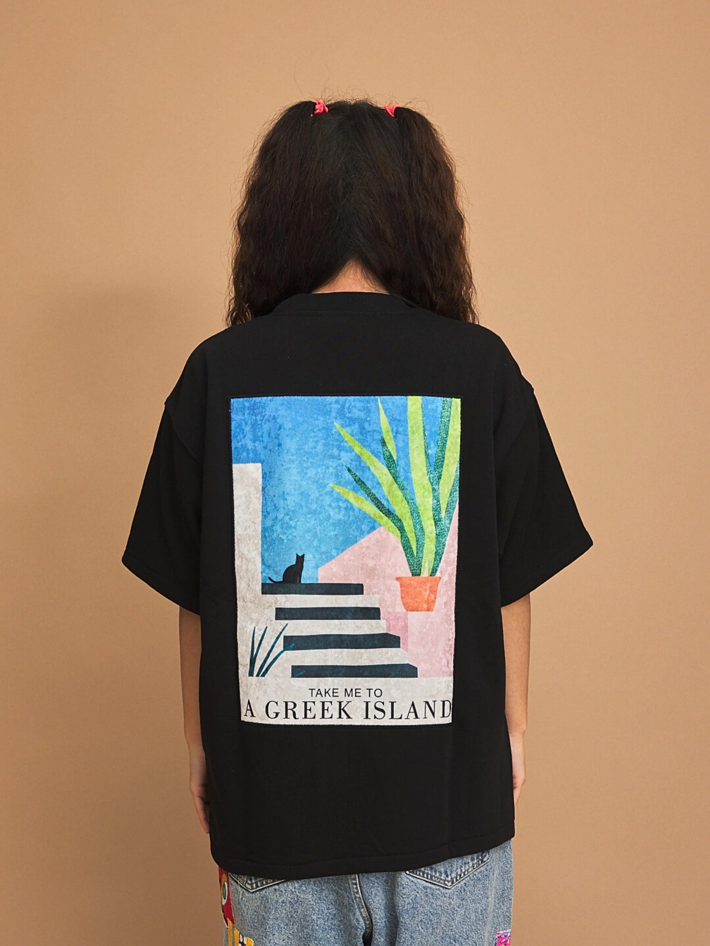 Person wearing a black t-shirt with a graphic design on the back against a brown background