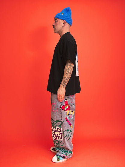 Person wearing a black t-shirt, colorful pants, and a blue beanie on an orange background