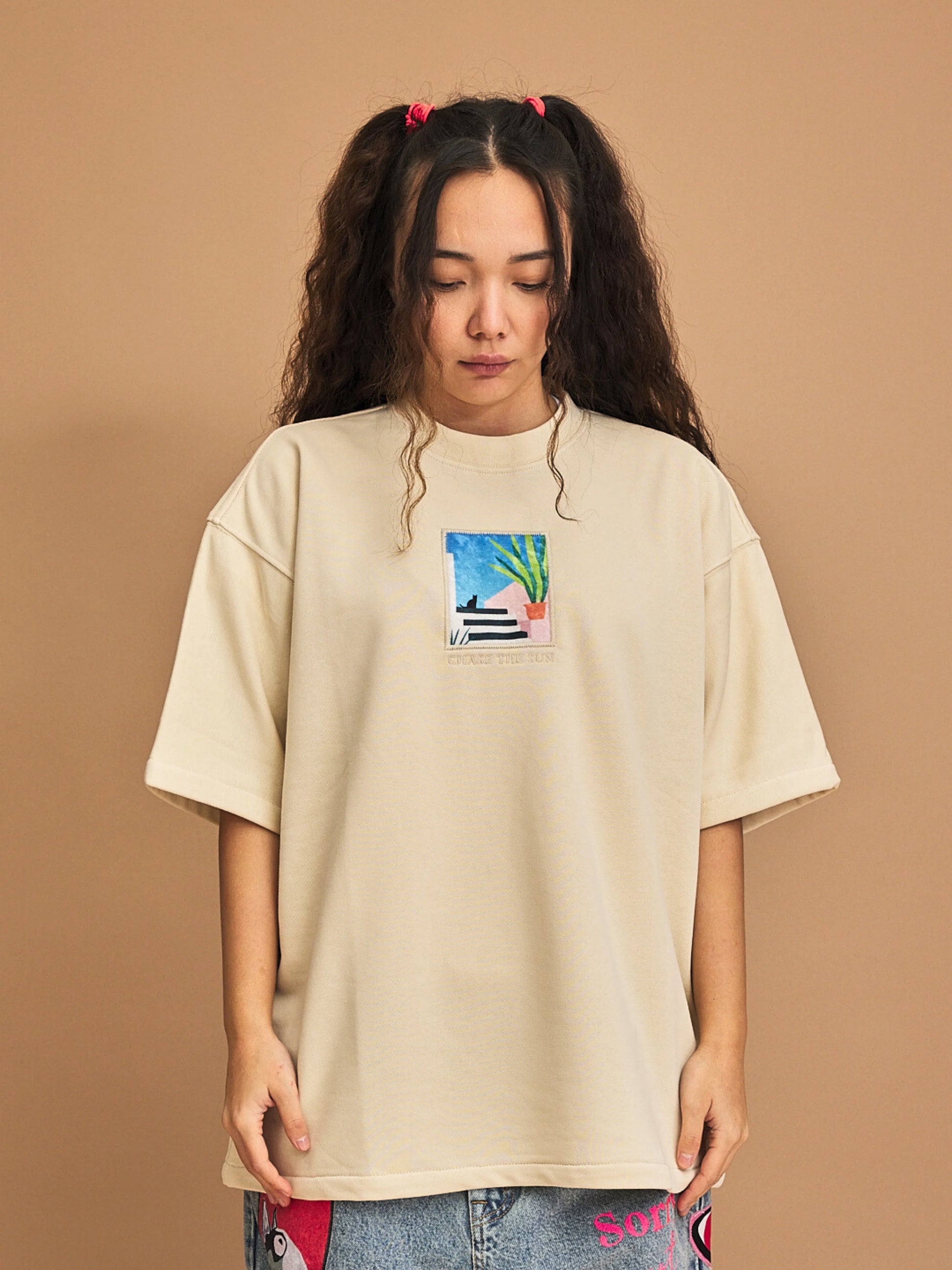 Person wearing a beige t-shirt with a colorful graphic on a brown background