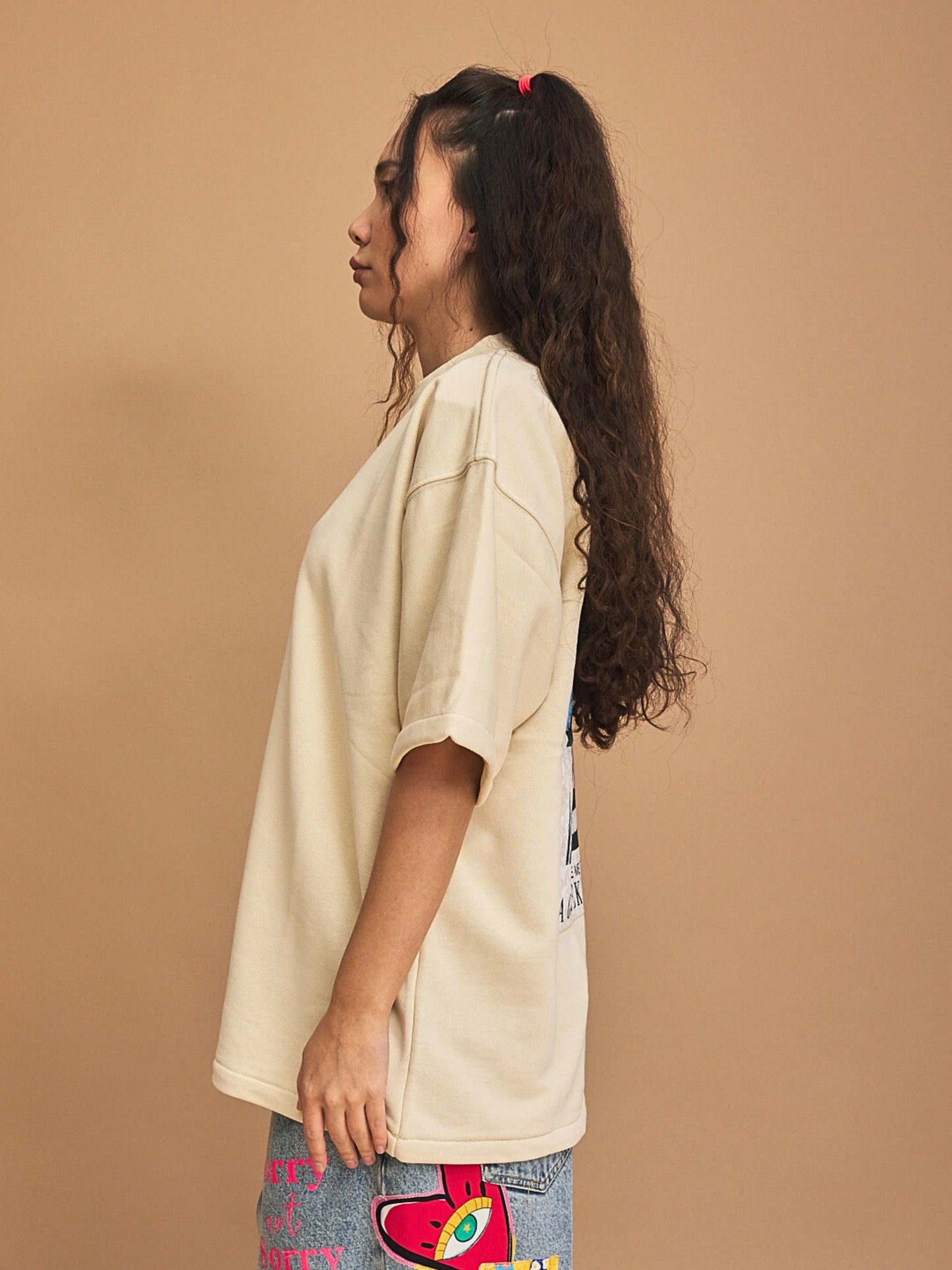 Woman wearing a beige oversized t-shirt against a brown background