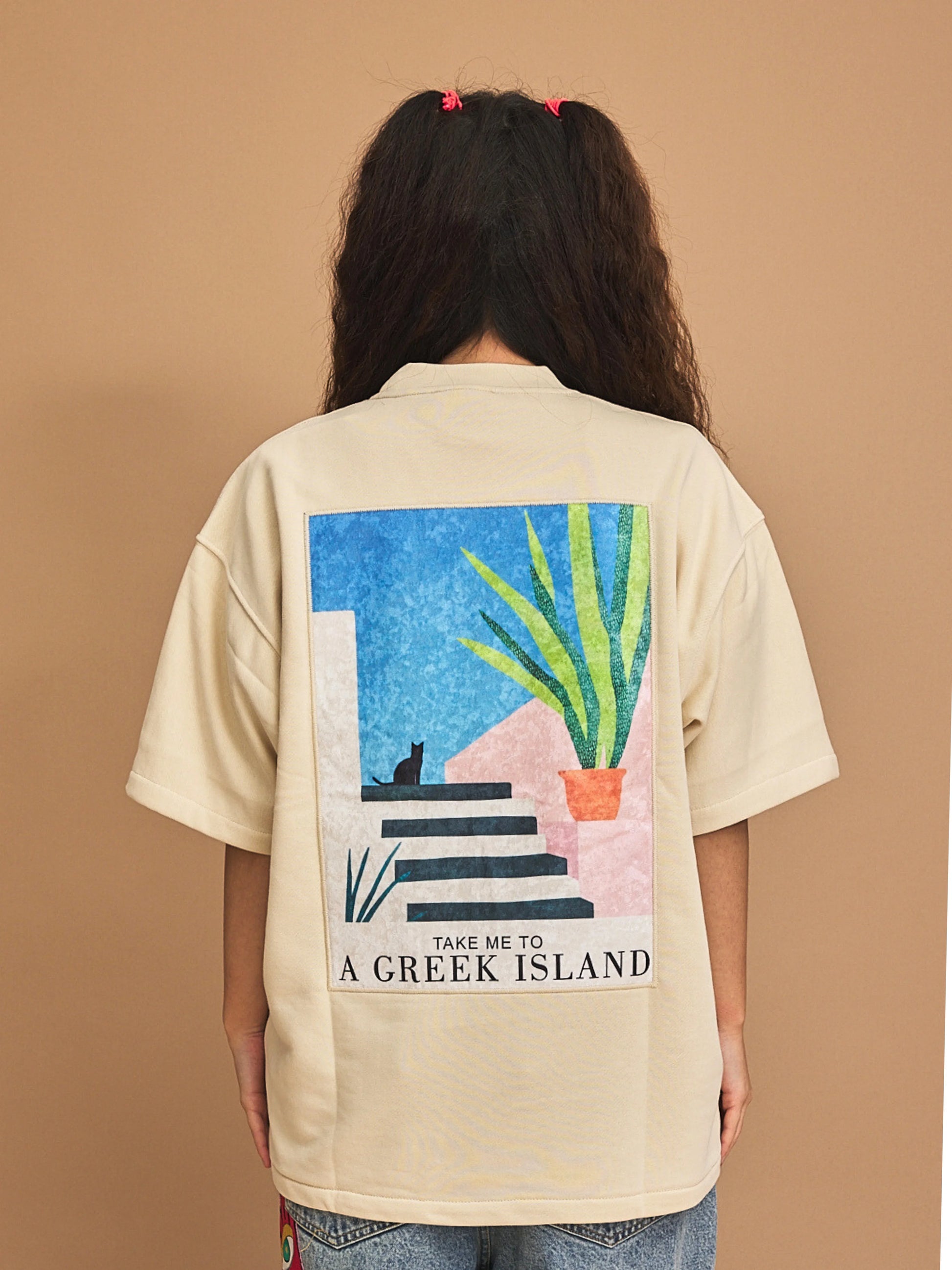 Person wearing a beige shirt with a graphic design and text on the back, against a brown background