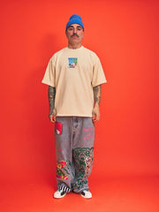 Person wearing a beige t-shirt, gray pants with designs, and a blue beanie on an orange background