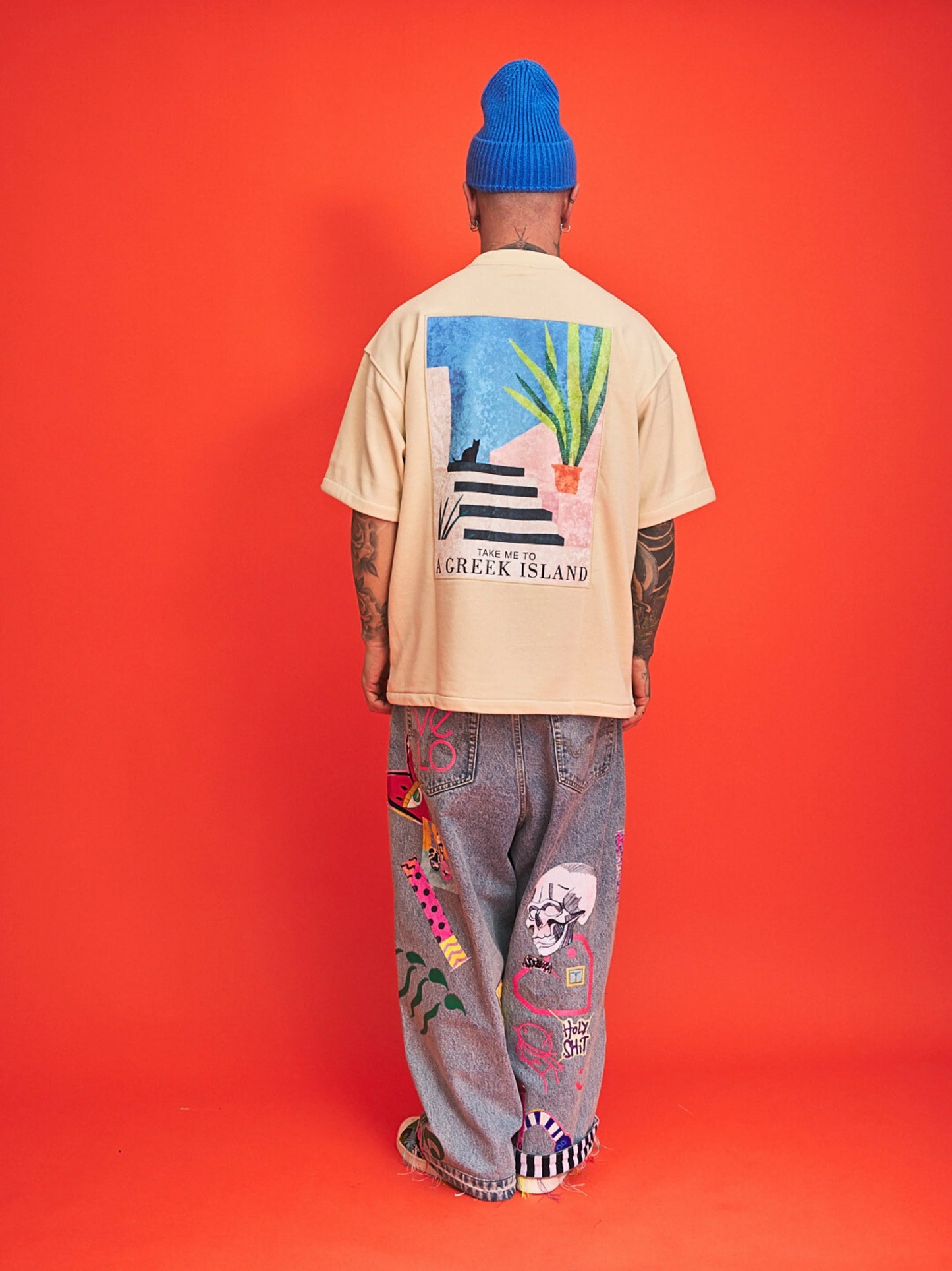 Person wearing a beige t-shirt with colorful graphics and text, standing against an orange background