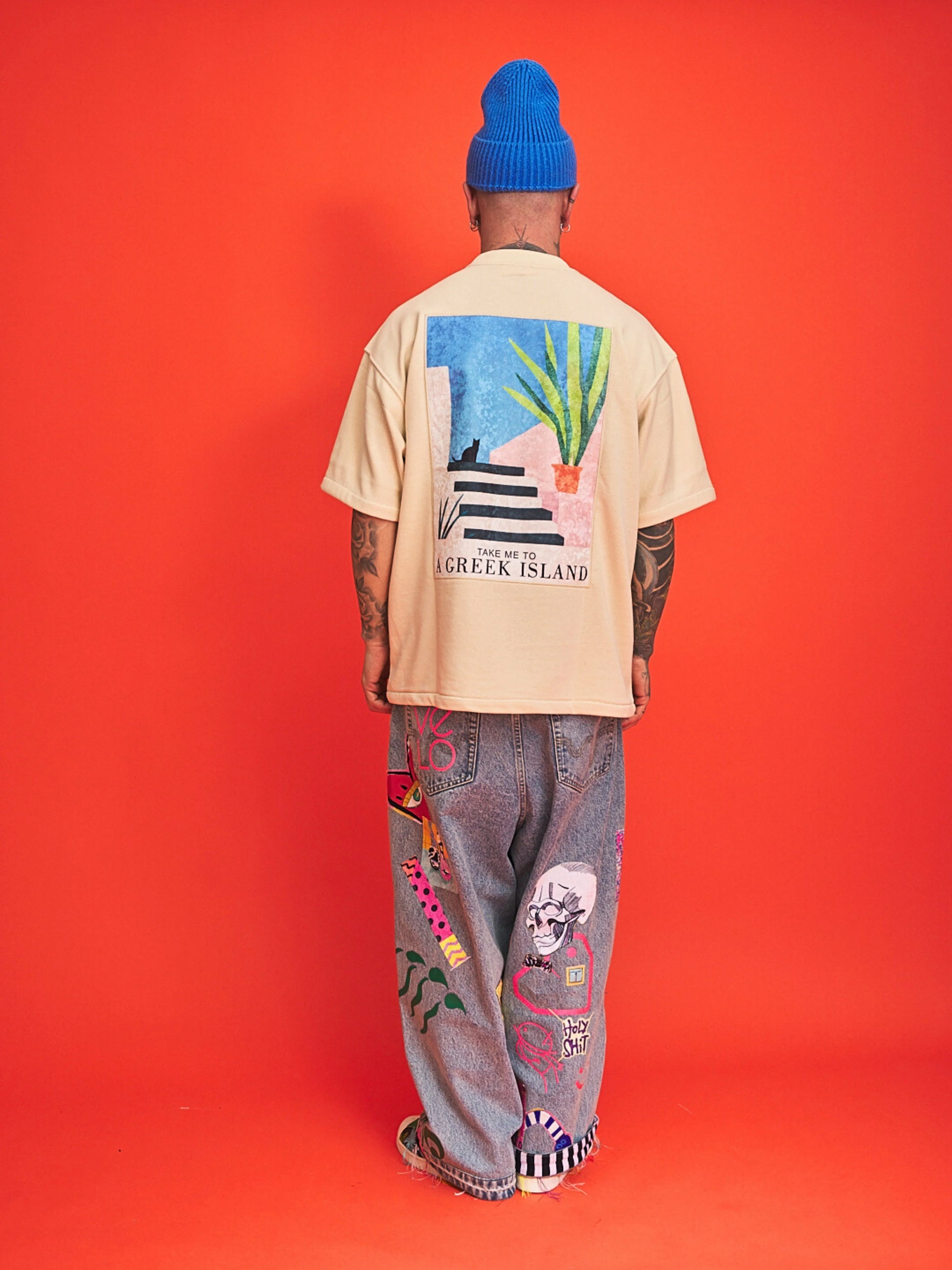 Person wearing a beige t-shirt with colorful graphics and text, standing against an orange background