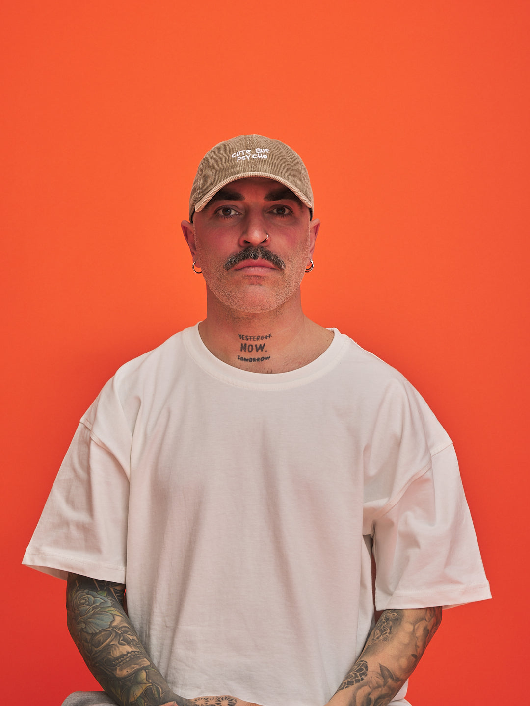 Man wearing a beige cap and white t-shirt against an orange background