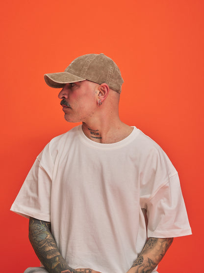 Person wearing a beige cap and white t-shirt against an orange background
