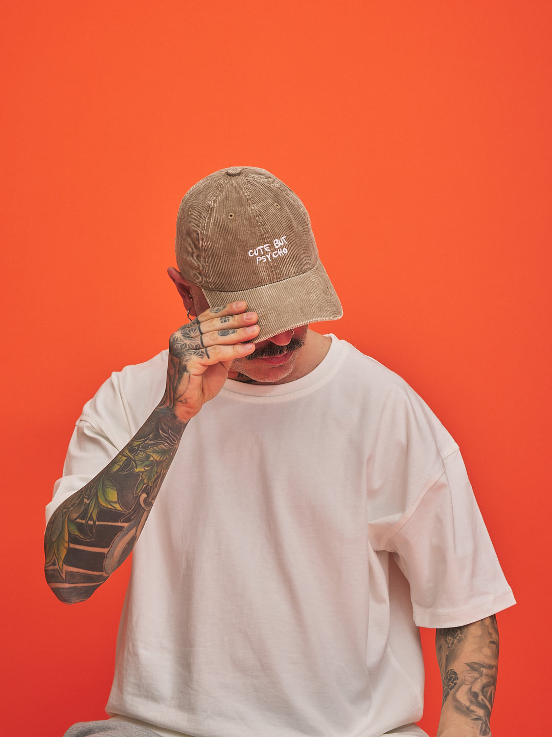Person wearing a beige cap and white t-shirt against an orange background