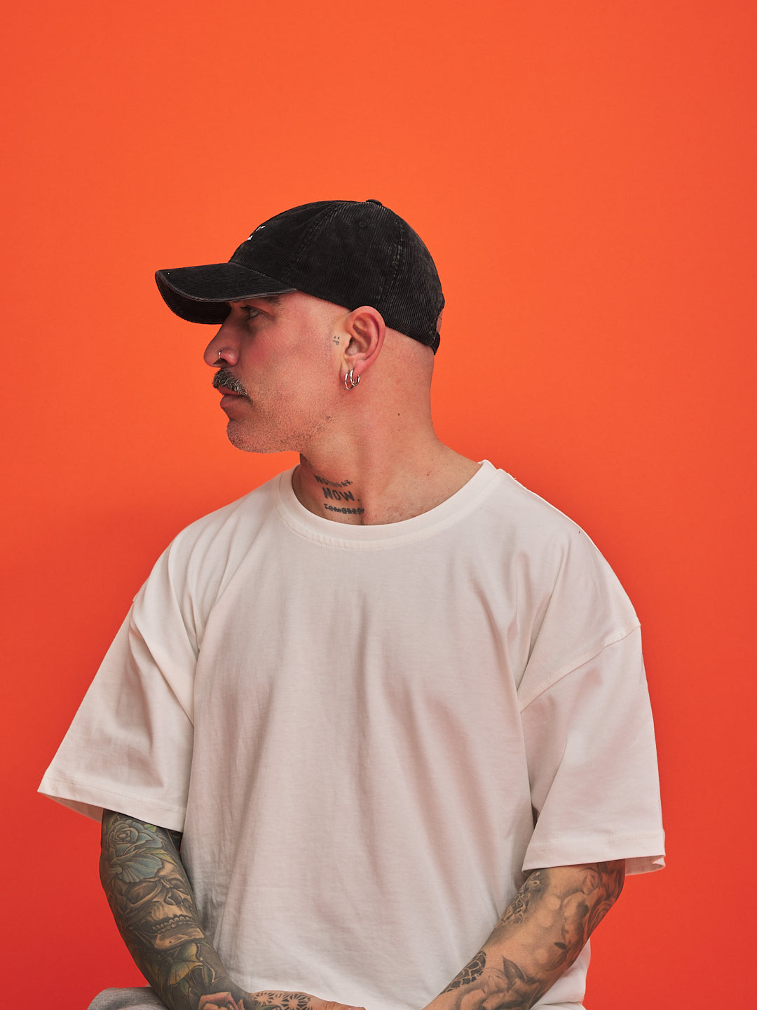 Man wearing a black cap and white t-shirt against an orange background