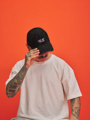 Person wearing a black cap with text and a white t-shirt against an orange background