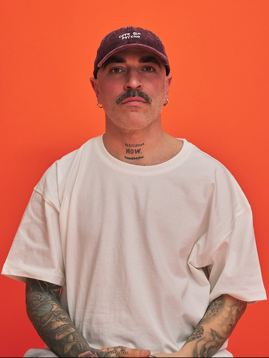 Man wearing a white t-shirt and corduroy cap against an orange background
