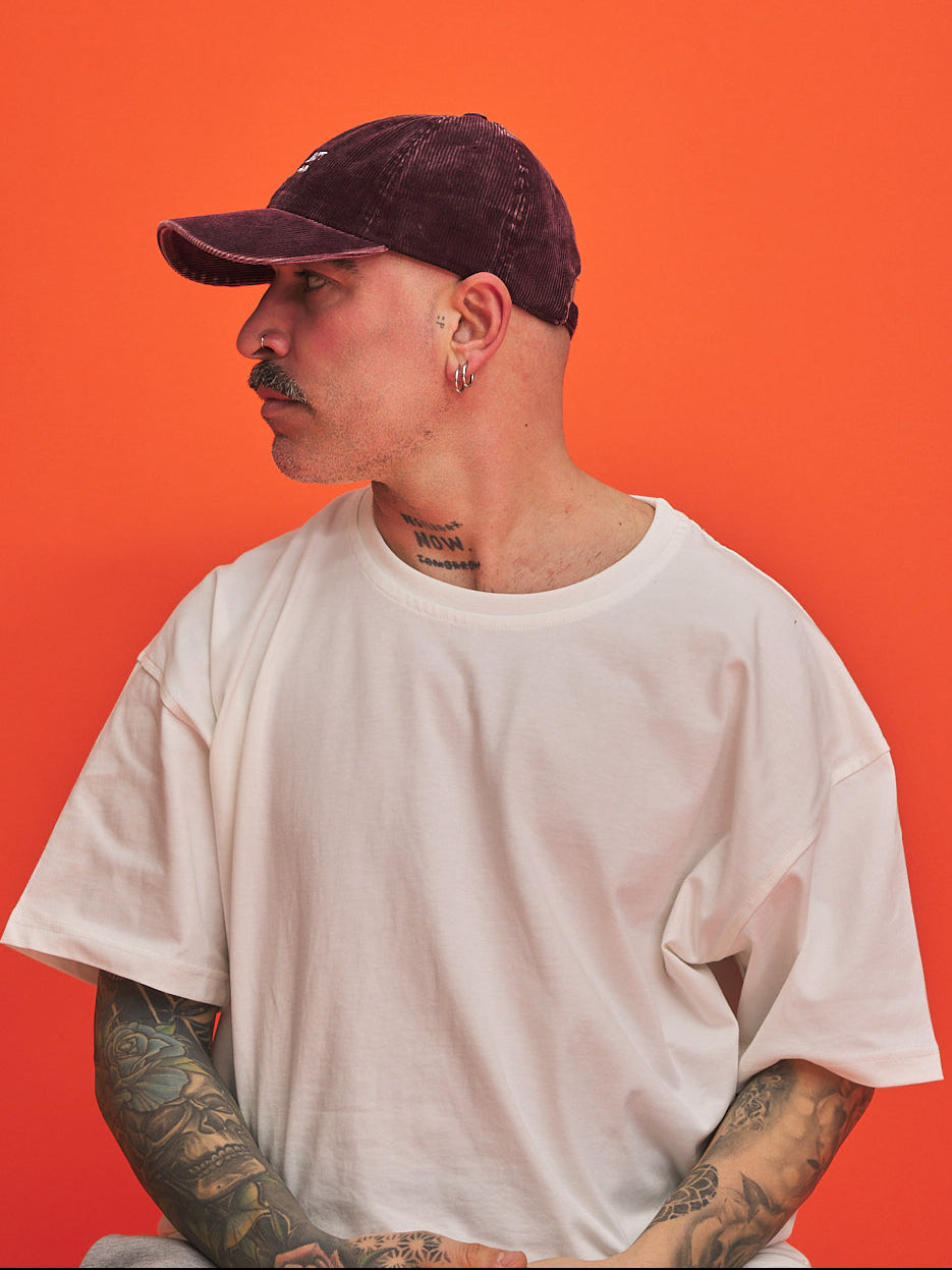 Person wearing a white t-shirt and dark cap against an orange background