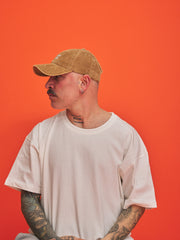 Person wearing a camel cap and white t-shirt against an orange background