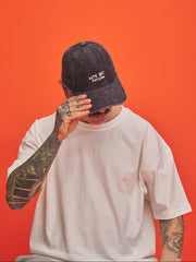 Man model covering his face with a charcoal grey cap with 'Cute But Psycho' text on an orange background