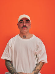Man wearing a cream corduroy cap and t-shirt against an orange background