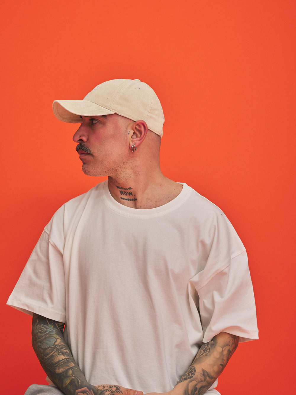 Man wearing a cream corduroy cap and white t-shirt against an orange background