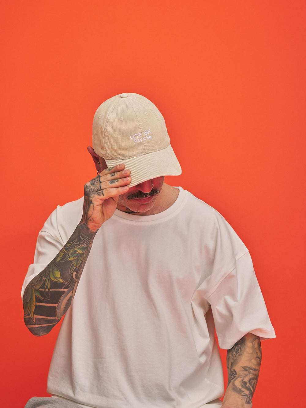 Person wearing a cream corduroy cap and white t-shirt against an orange background