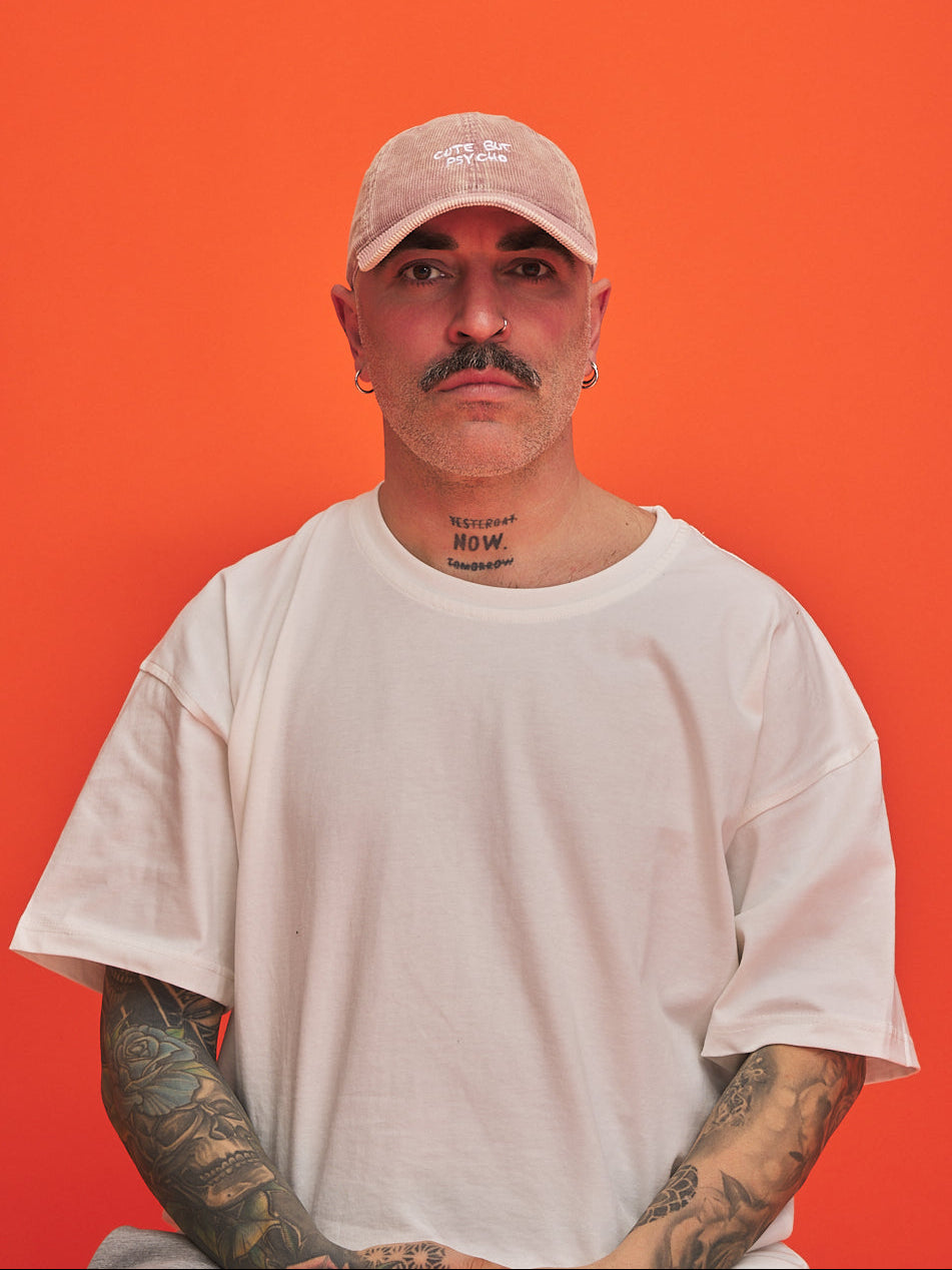 Man wearing a beige cap and white t-shirt against an orange background
