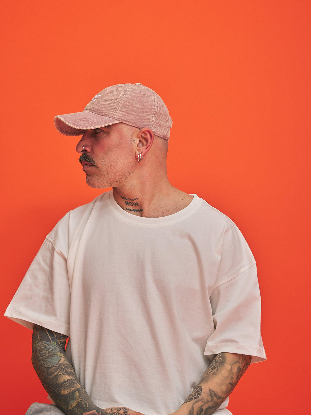 Person wearing a dusty pink cap and white t-shirt against an orange background