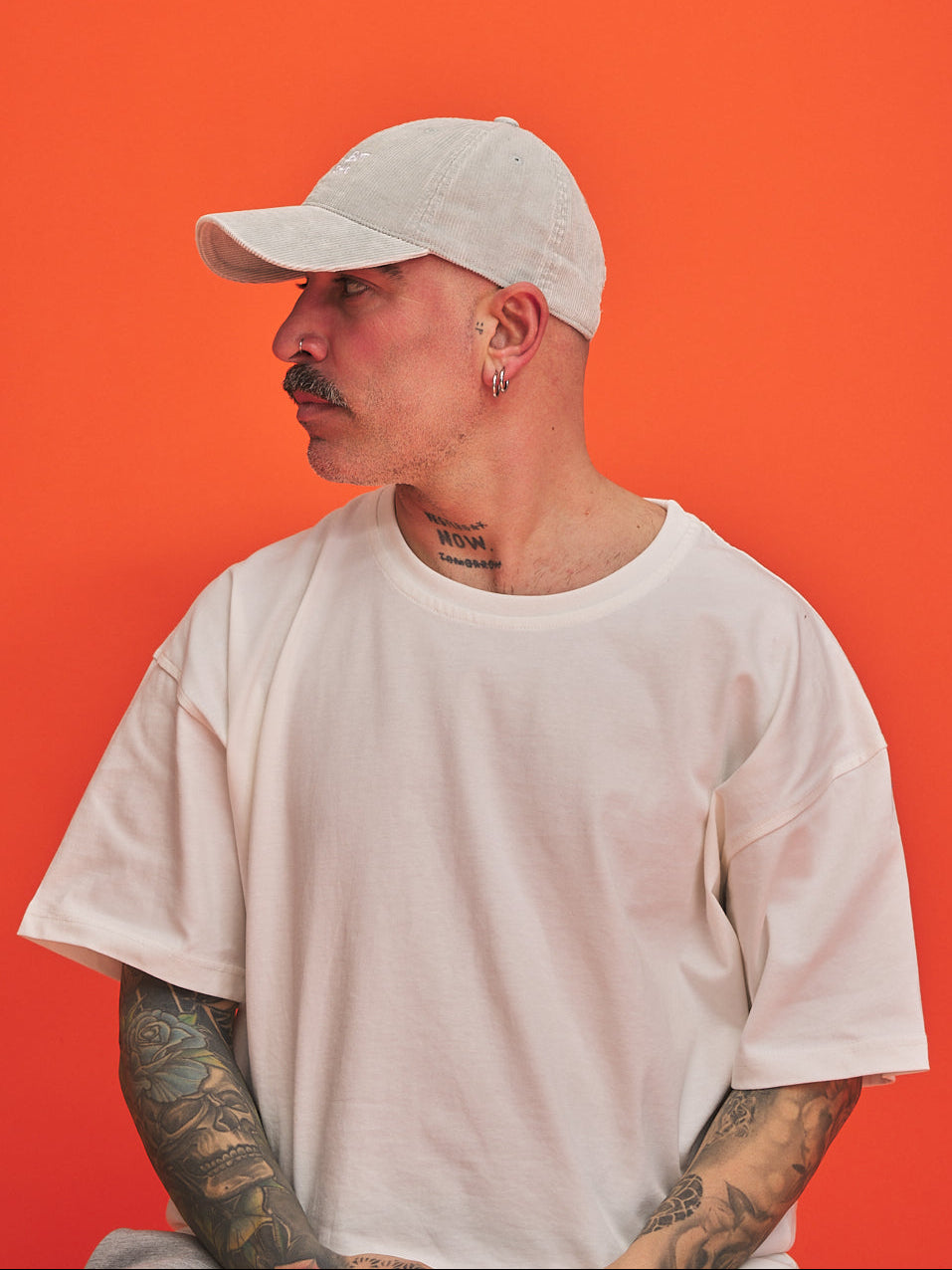 Man wearing a light grey cap and t-shirt against an orange background