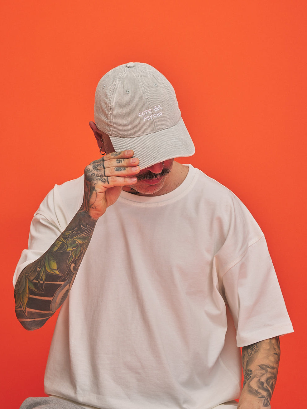 Person wearing a light grey cap and white t-shirt against an orange background