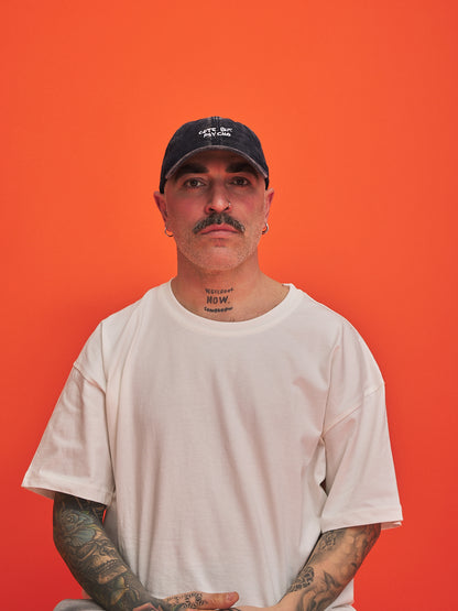 Man wearing a white t-shirt and navy corduroy cap against an orange background