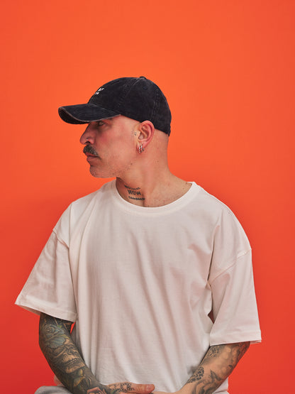 Person wearing a navy corduroy cap and white t-shirt against an orange background