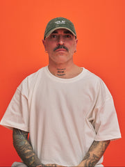 Front look of man wearing a green corduroy cap and white t-shirt against an orange background