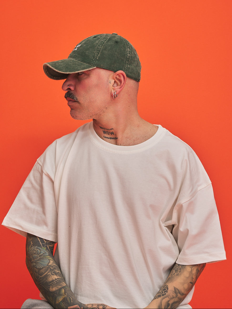 Side look of man wearing a olive green cap and white t-shirt against an orange background