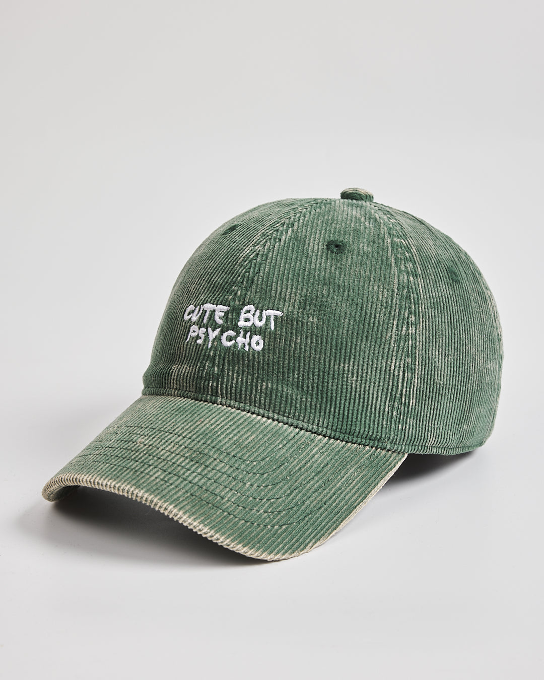 Green corduroy cap with 'Cute But Psycho' text on a light gray background