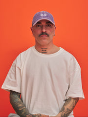 Man wearing a purple cap and white t-shirt against an orange background