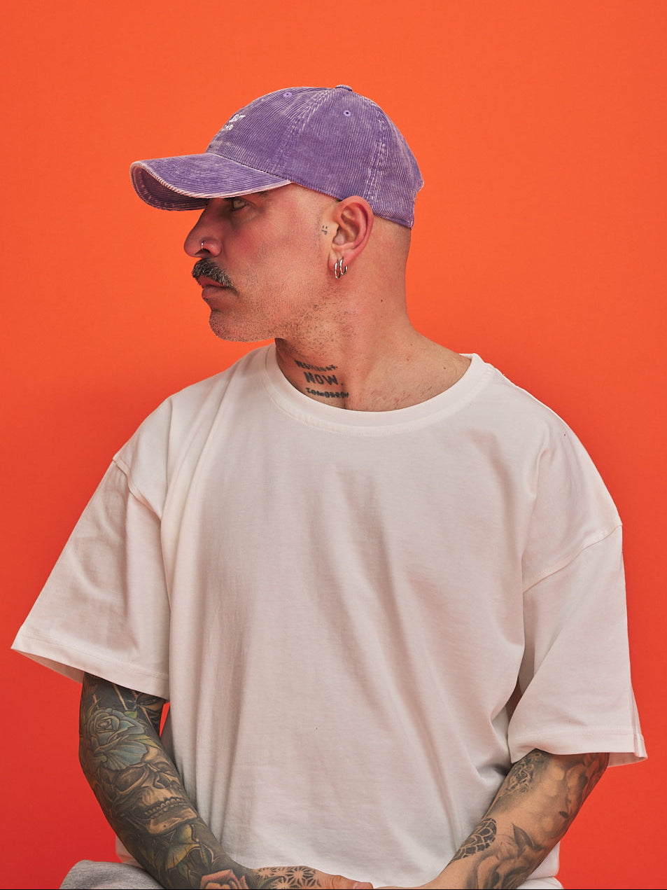 Person wearing a purple cap and white t-shirt against an orange background
