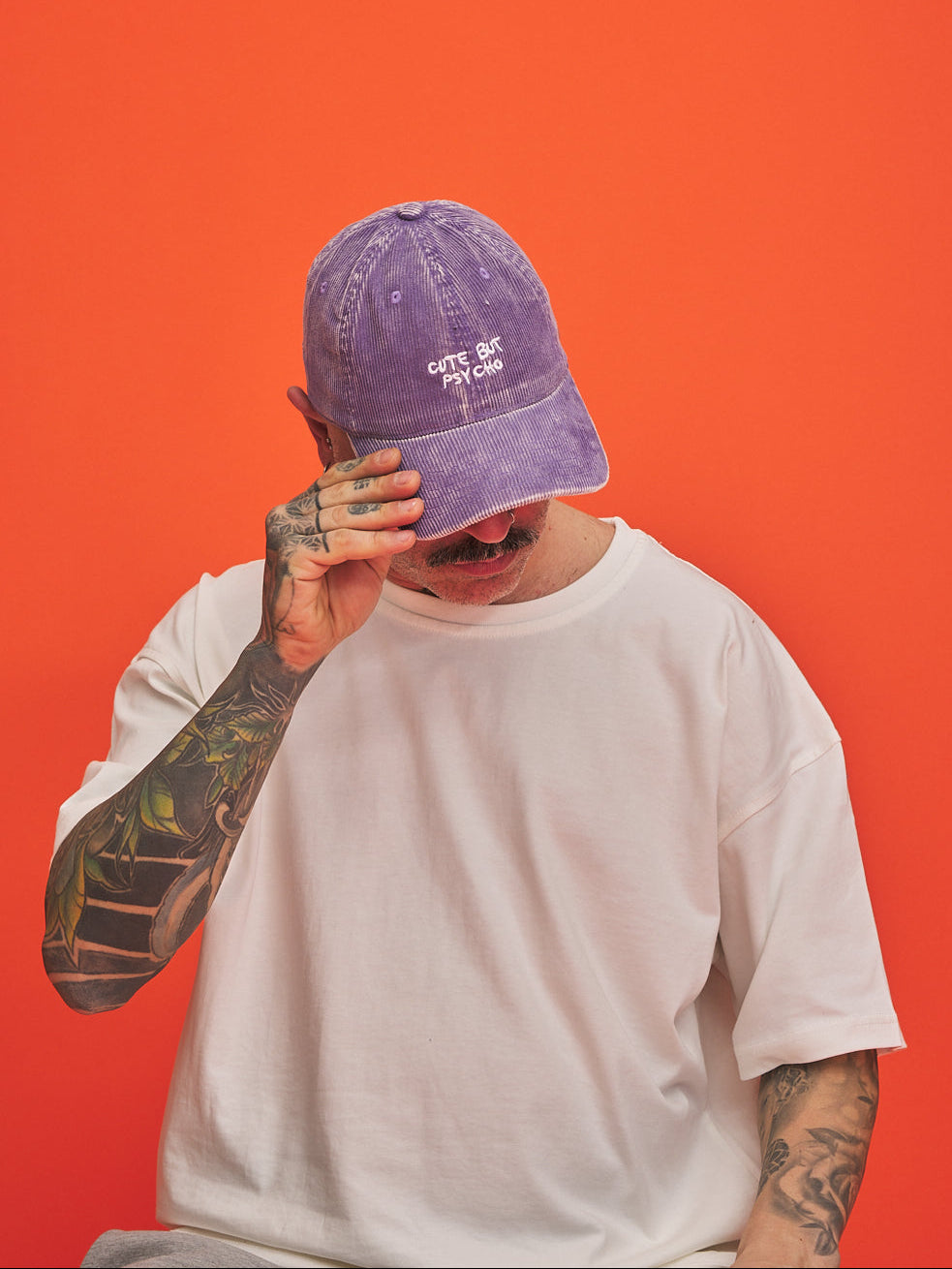 Person wearing a purple cap and white t-shirt against an orange background