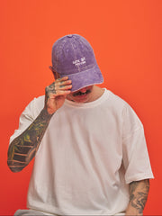 Person wearing a purple cap and white t-shirt against an orange background