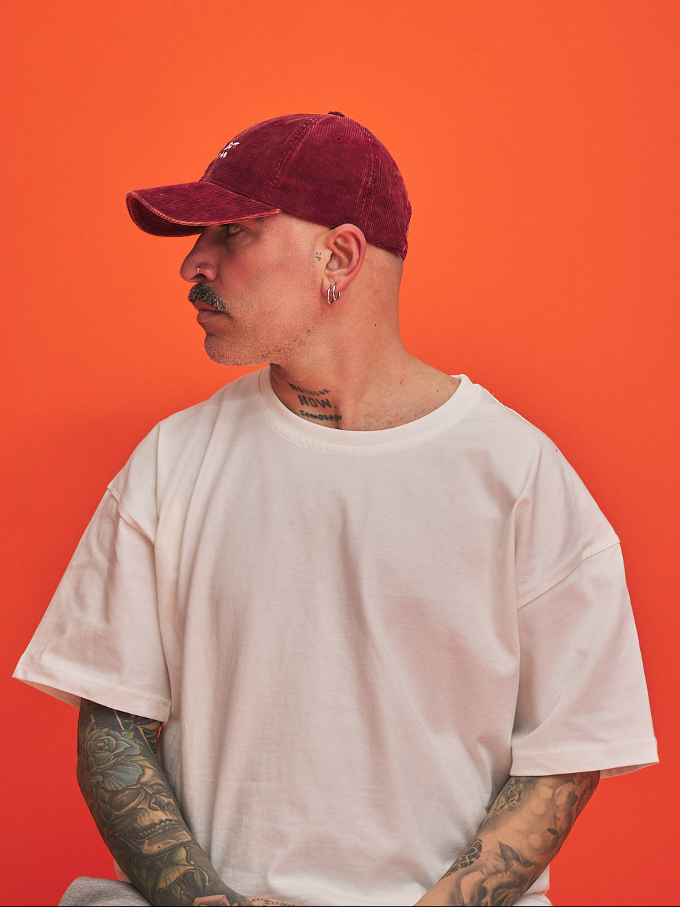 Person wearing a corduroy cap and white t-shirt against an orange background