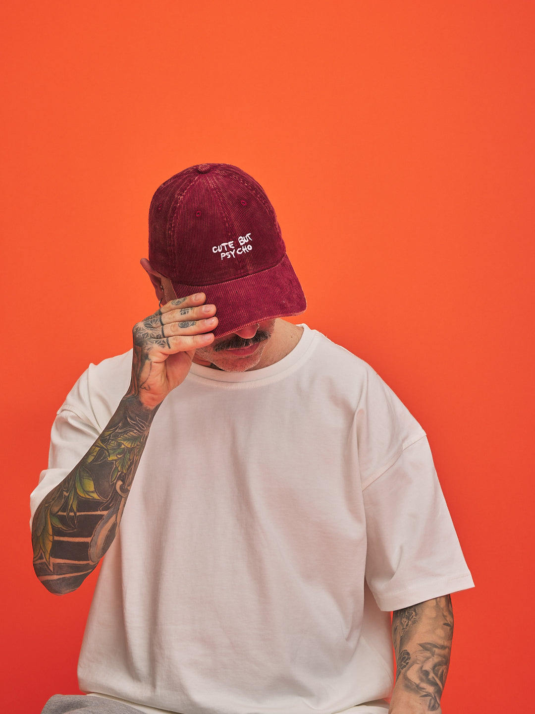 Person wearing a red corduroy cap with Cute But Psycho text on an orange background