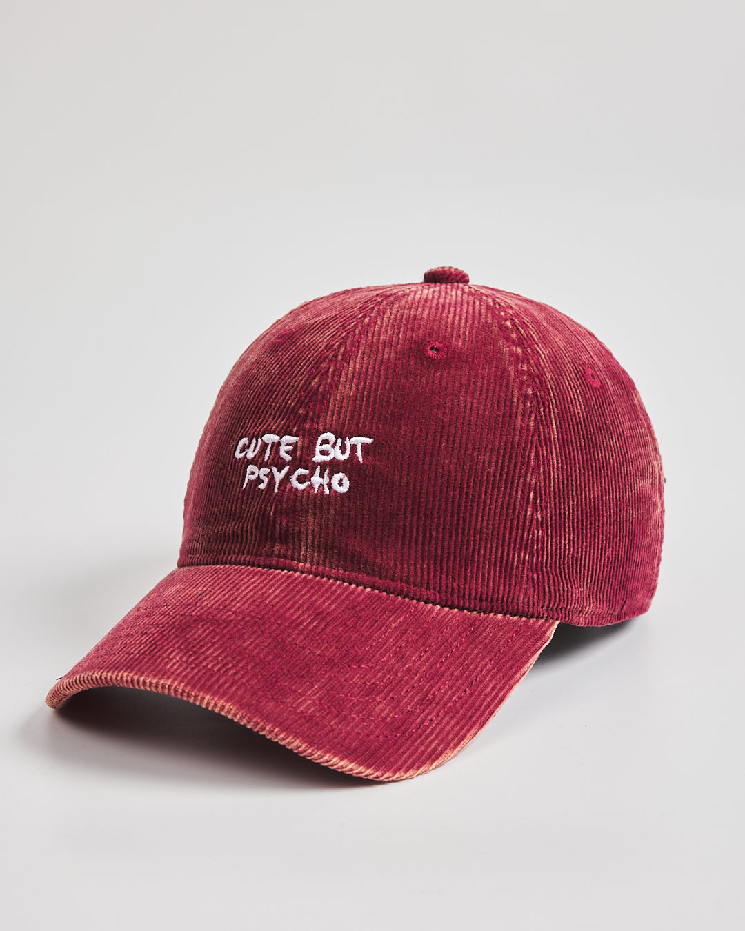 Red corduroy cap with 'Cute But Psycho' text on a light gray background