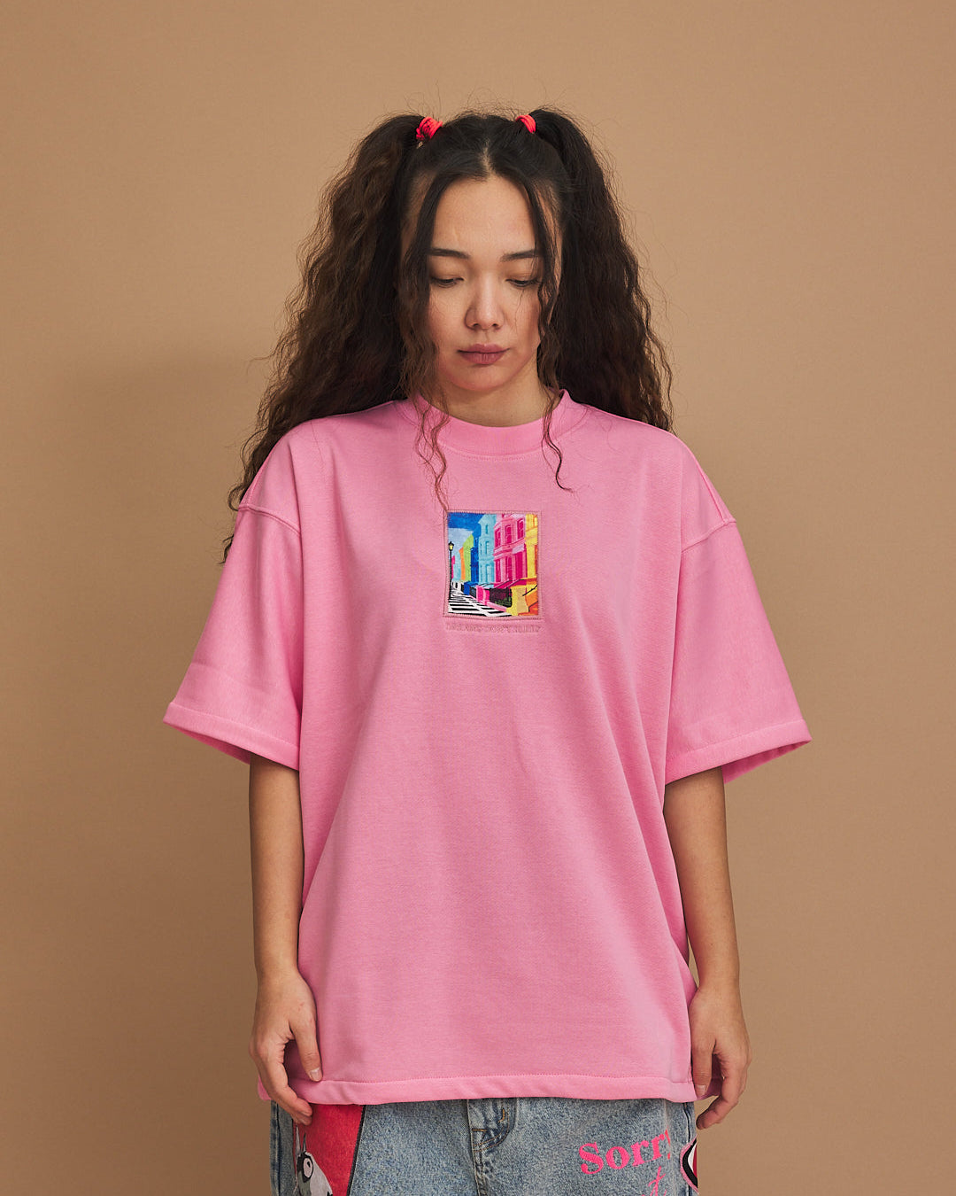 Person wearing a pink oversized t-shirt with a colorful graphic on a brown background