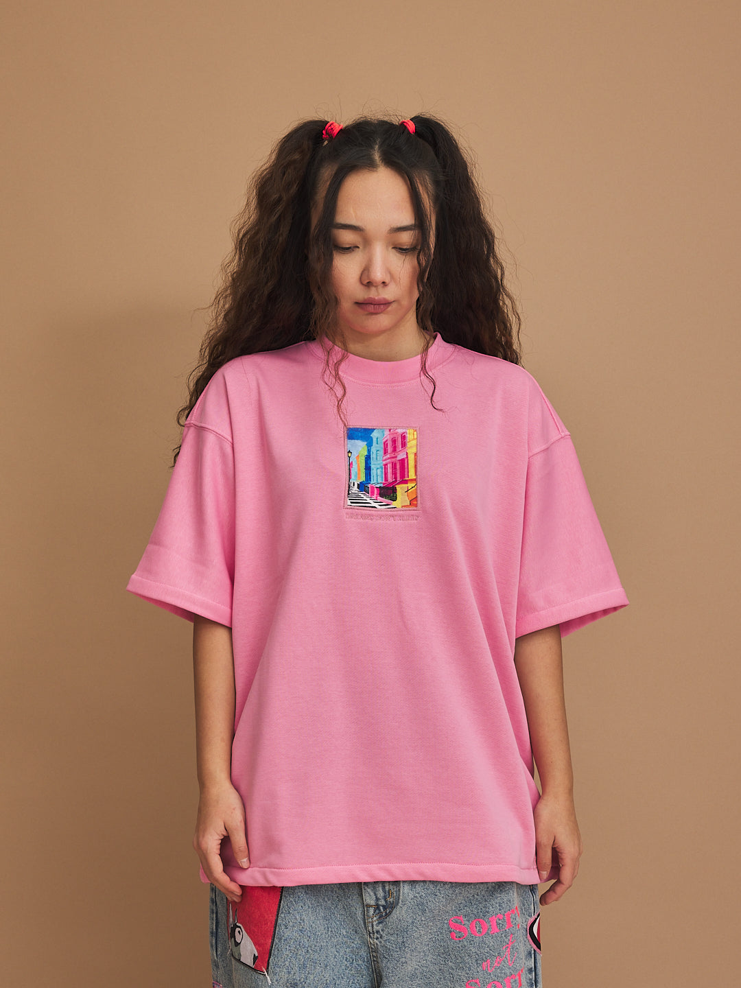 Person wearing a pink oversized t-shirt with a colorful graphic on a brown background
