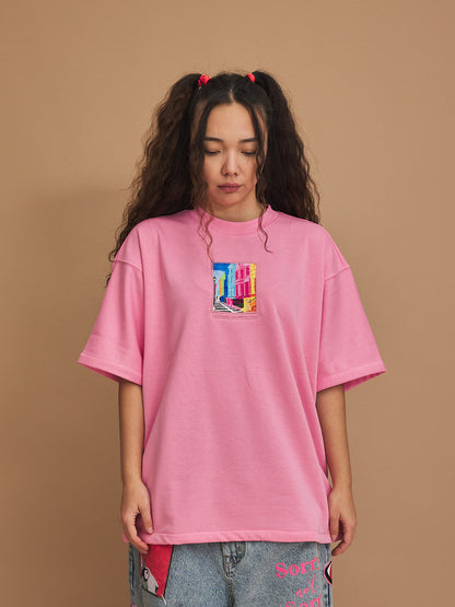 Person wearing a pink oversized t-shirt with a colorful graphic on a brown background